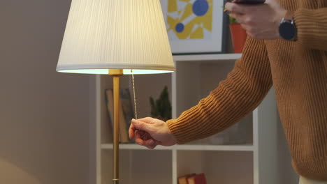 man-is-turning-off-floor-lamp-in-living-room-or-bedroom-at-evening-interior-of-modern-apartment-closeup-view